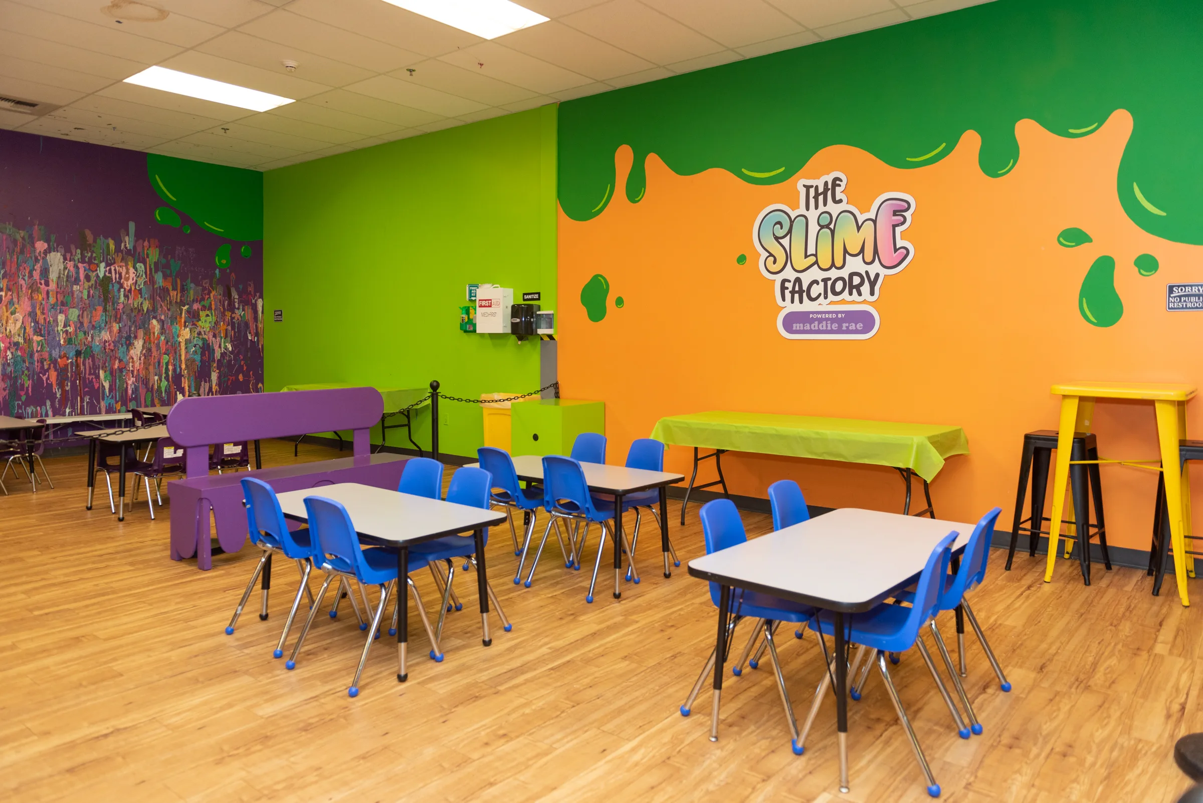 Bellevue’s single party area with blue tables and chairs, purple benches, a green wall, and the orange Slime Factory logo wall.