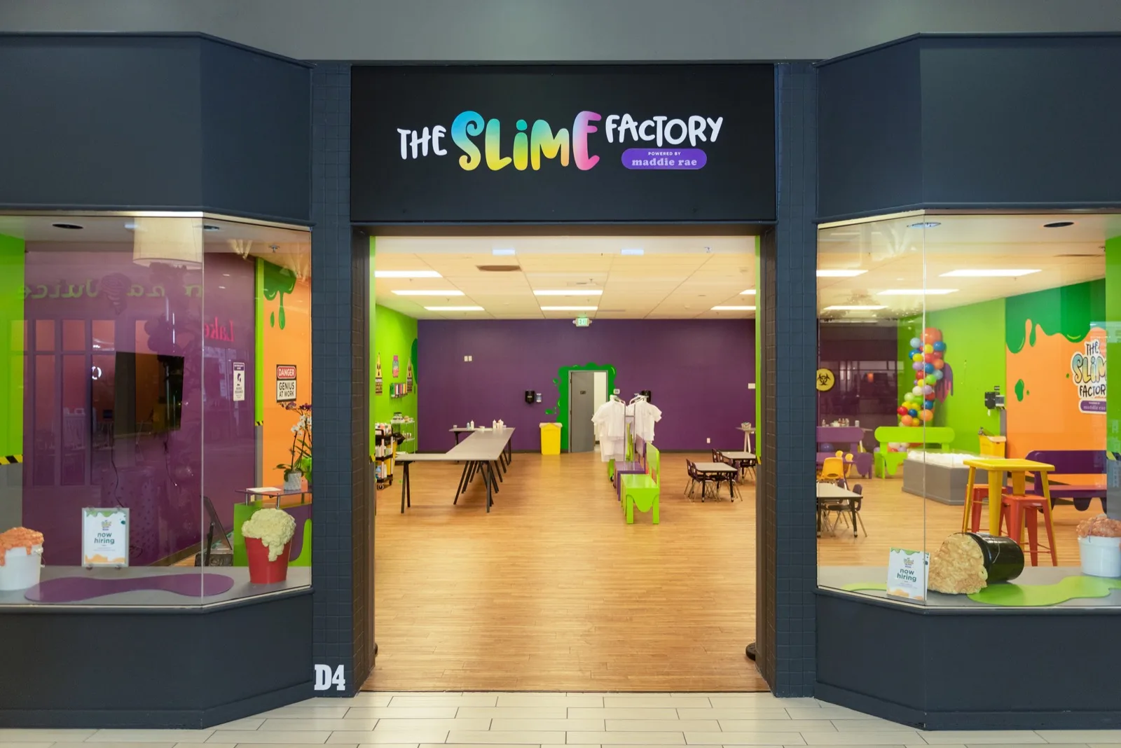 The Bellevue Slime Factory entrance, with a black rainbow-lettered sign, glass display windows, the D4 unit marker, and colorful lab walls inside.