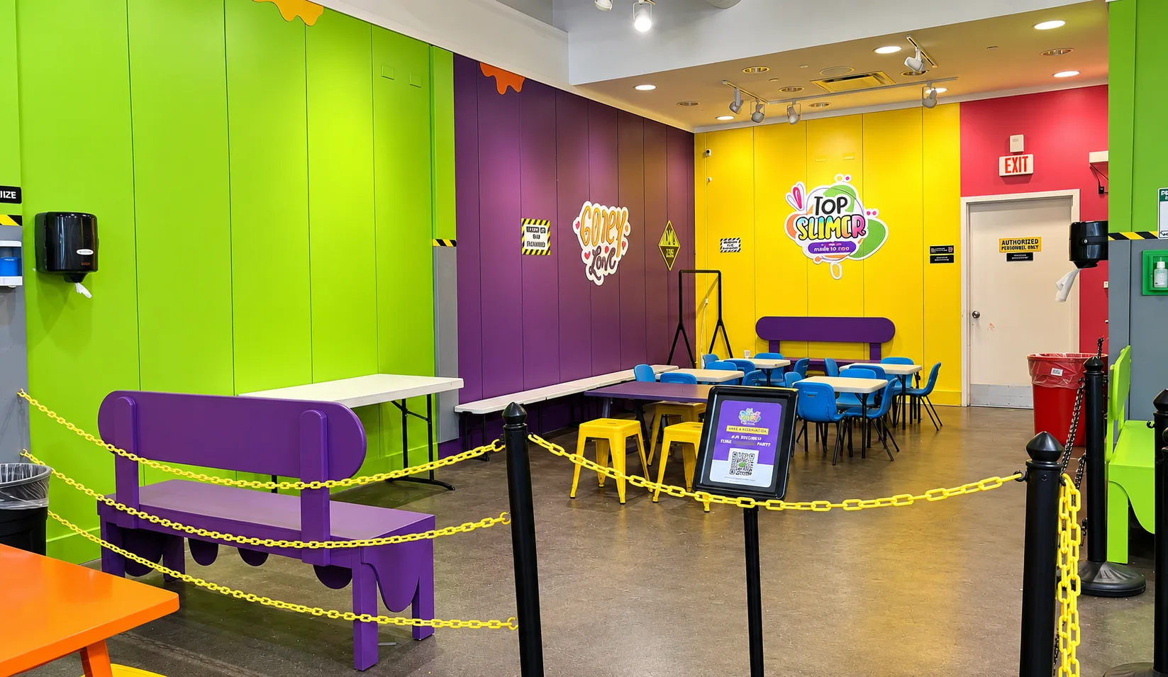 Edison’s large party area with the Top Slimer sign on a yellow wall, blue chairs, and a purple bench.