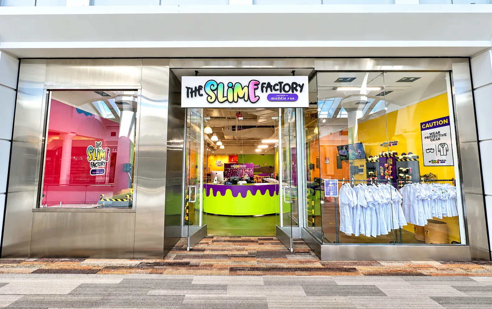 The Slime Factory entrance at Menlo Park Mall, with a rainbow sign, glass doors, and lab coats beside the entrance.