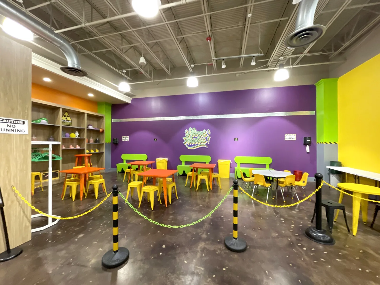 Alpharetta’s large party area with a purple wall, orange tables, yellow chairs and green benches.