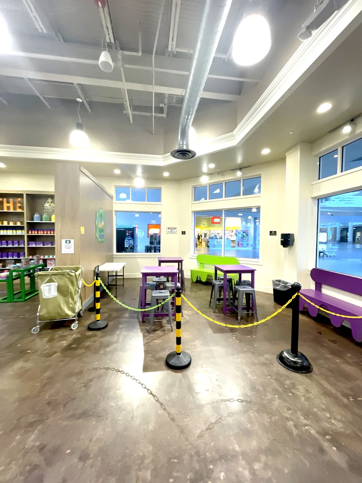 Alpharetta’s small party area beside the mall-facing windows, with purple tables, stools and colorful benches.