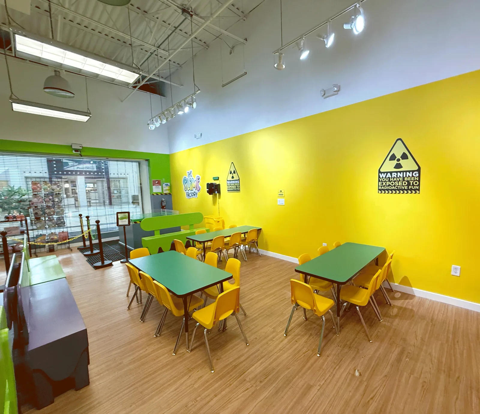 Miami’s single party area with green tables, yellow chairs, a lime bench, and bright yellow walls beside the storefront windows.