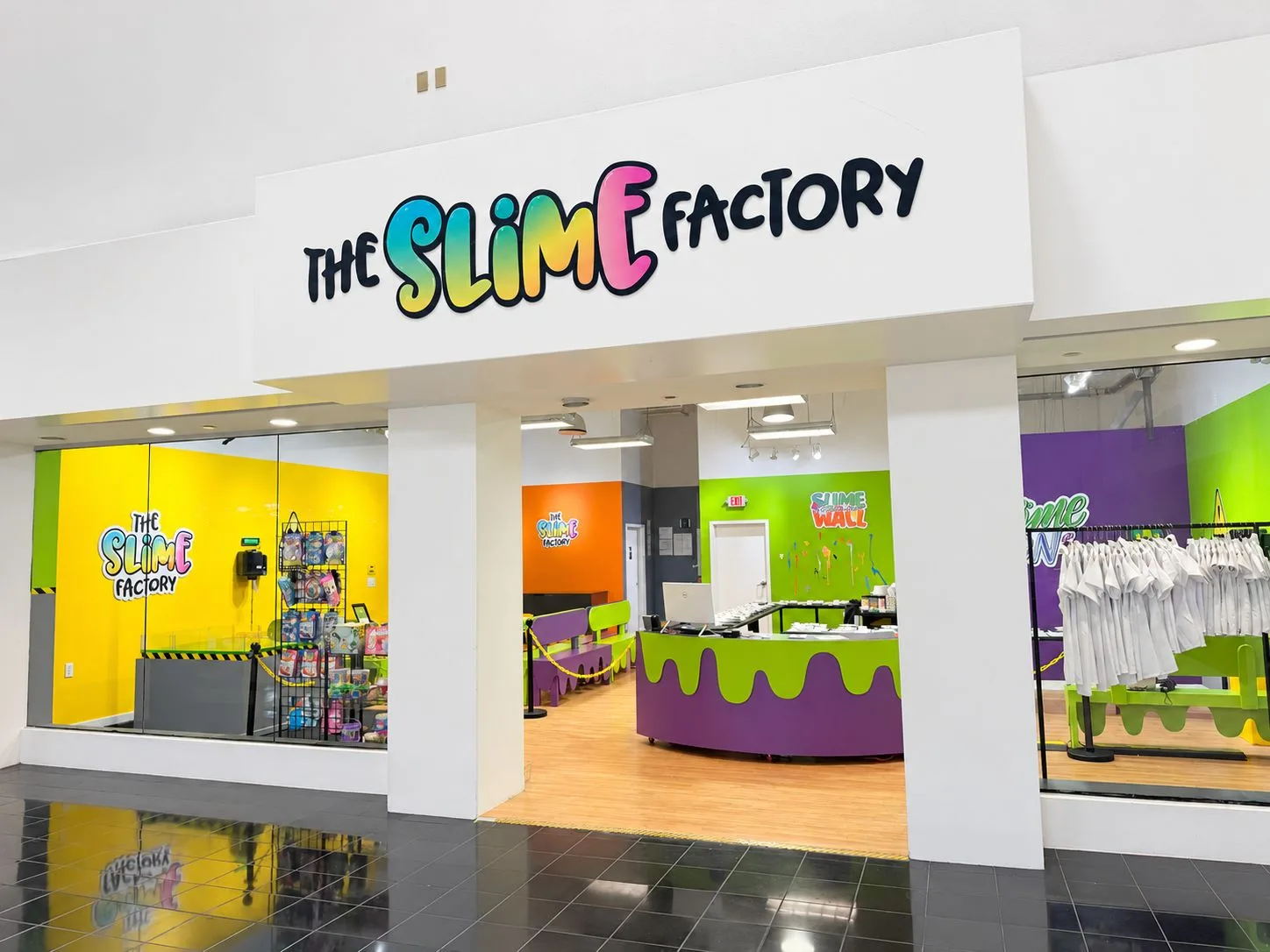 The Slime Factory entrance at Miami International Mall, with a large rainbow sign, purple and lime reception desk, and white lab coats.