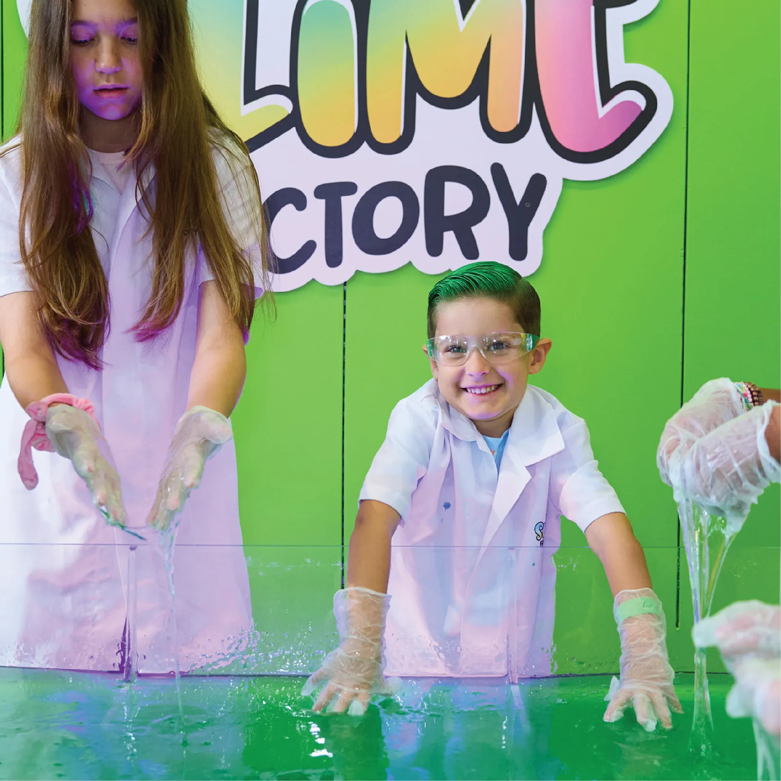 Young guests in white lab coats stretch green slime over the slime pool.
