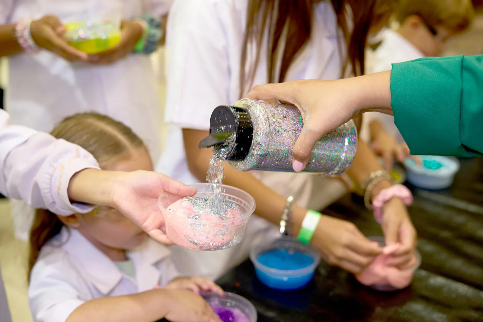 A child holds a container of pink slime as sparkling glitter is poured over it.