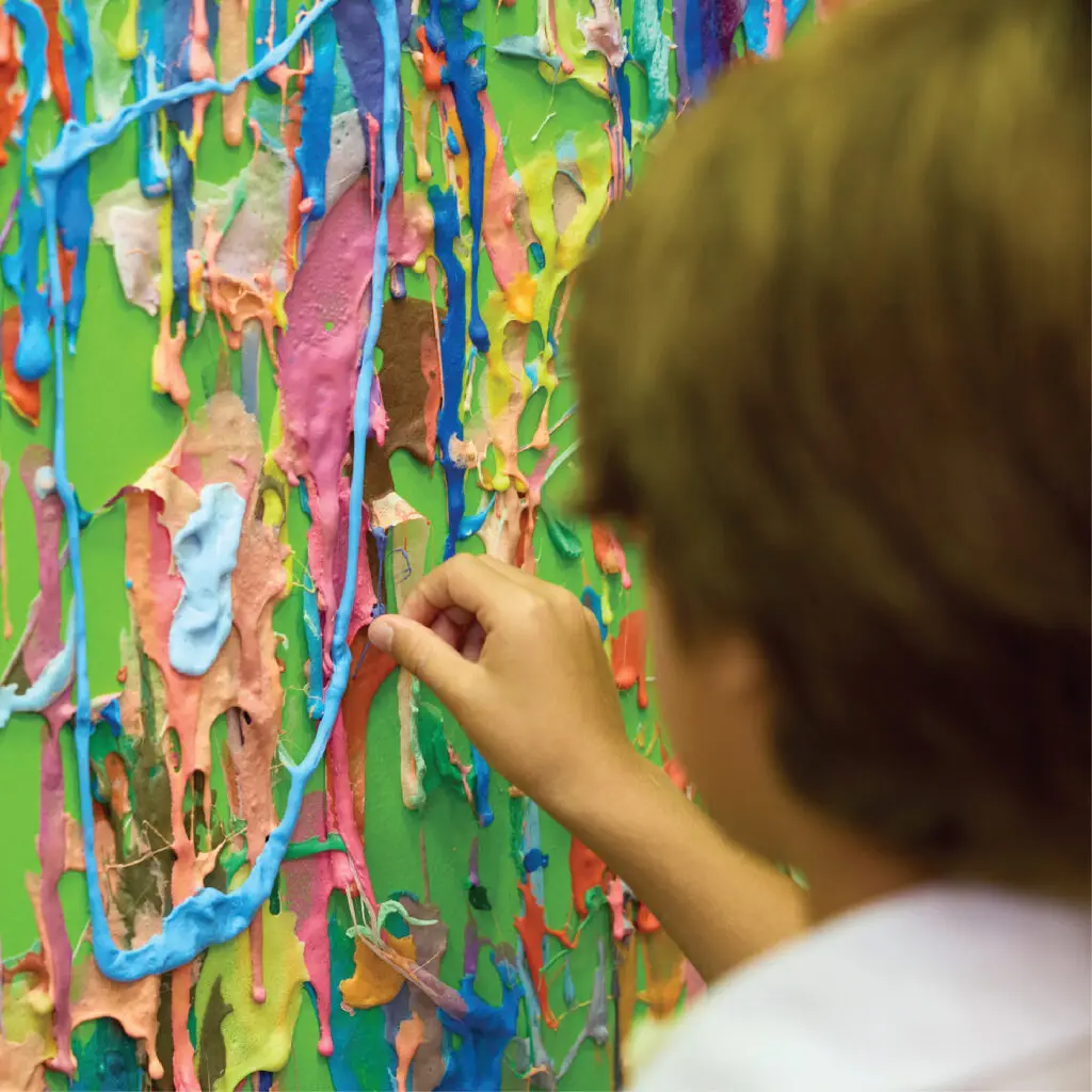 A child reaches into a wall of colorful dripping slime